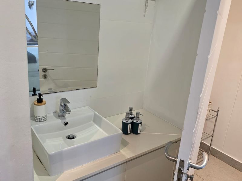 A compact bathroom featuring a modern vessel sink, vanity cabinet, and wall-mounted mirror with a venetian blind.