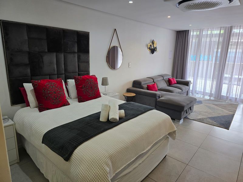 A spacious bedroom featuring tiled flooring, recessed lighting, a ceiling-mounted air conditioning unit, and direct access to a balcony through sliding glass doors.
