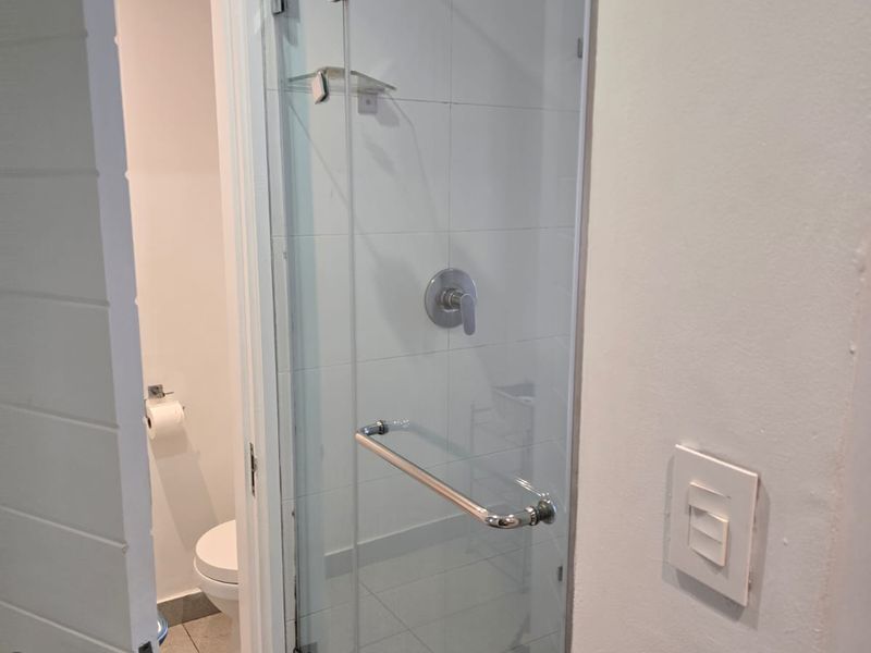 A clean bathroom featuring a glass-enclosed shower with modern fixtures and a separate toilet area with tiled finishes.