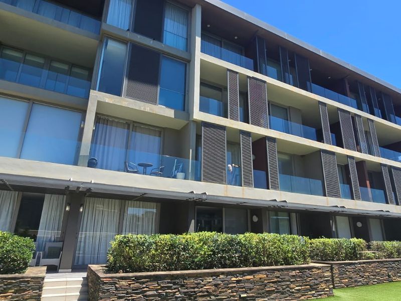 Modern apartment building exterior featuring multi-level balconies with glass balustrades, stone-clad retaining walls, and integrated louvred shutters.