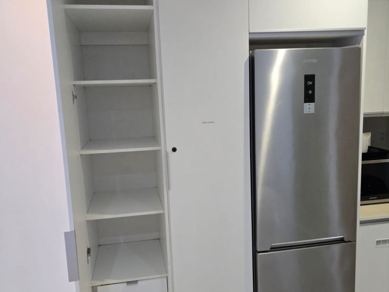 A modern kitchen featuring clean white built-in pantry cabinetry with integrated storage and a dedicated space for a refrigerator.