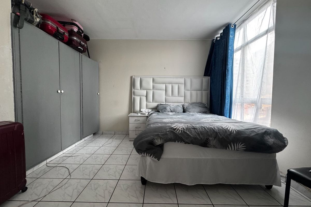 A bedroom featuring tiled flooring, a large window for natural light, and a built-in wardrobe providing ample storage space.