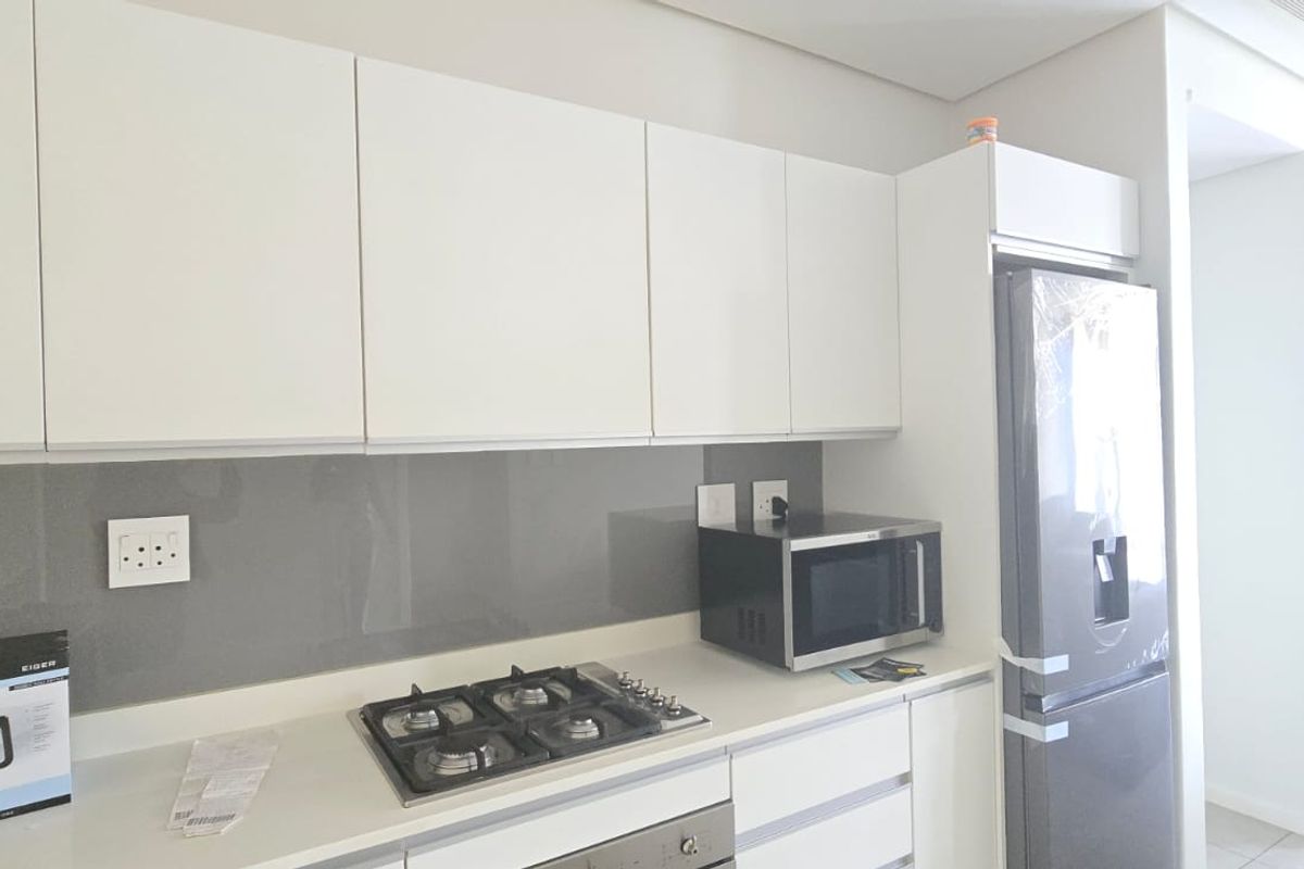 Modern kitchen featuring sleek white cabinetry, stone countertops, a glass splashback, and integrated gas hob with built-in oven.