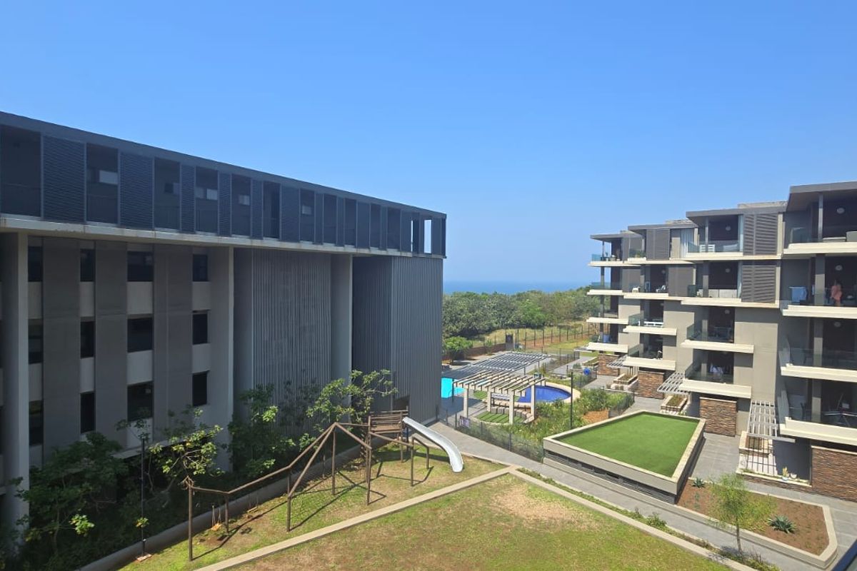 Elevated view of the apartment complex grounds featuring a swimming pool, landscaped garden areas, and modern building facades with private balconies.