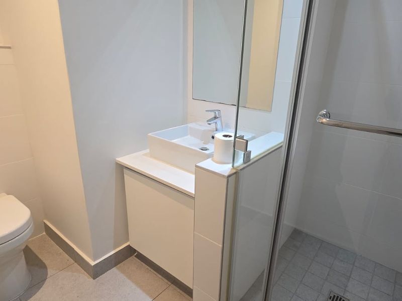A modern, clean bathroom featuring a wall-mounted toilet, a sleek vanity with a vessel sink, and a glass-enclosed shower with tiled flooring.
