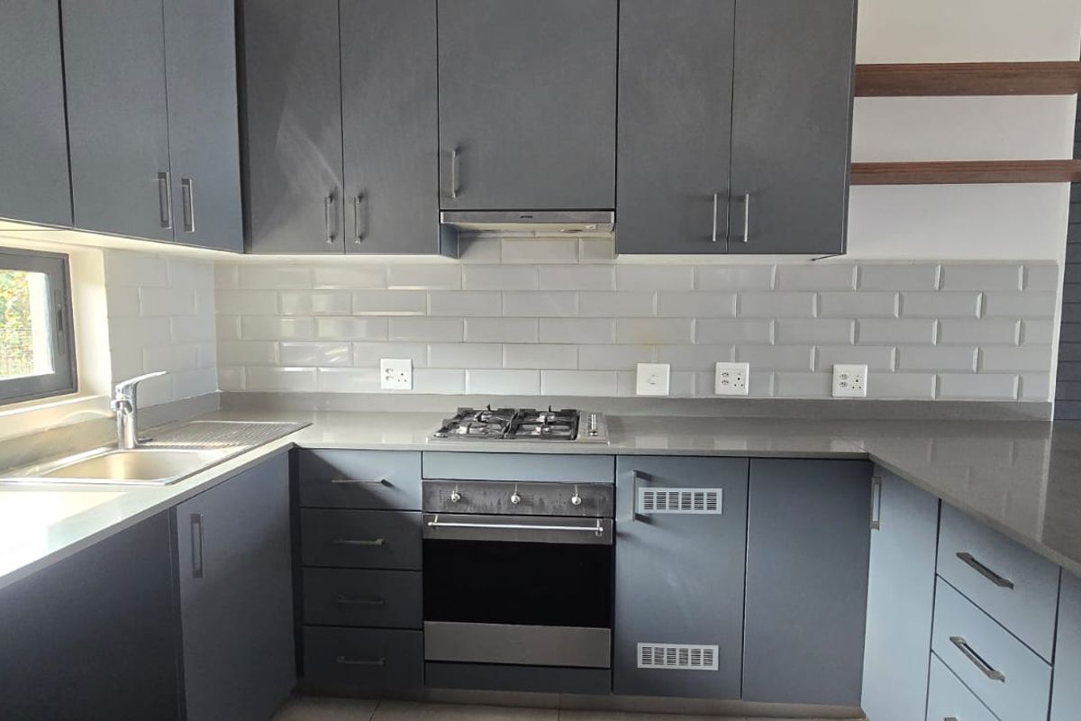 Modern kitchen featuring dark grey cabinetry, stone countertops, subway tile backsplash, and integrated stainless steel appliances.