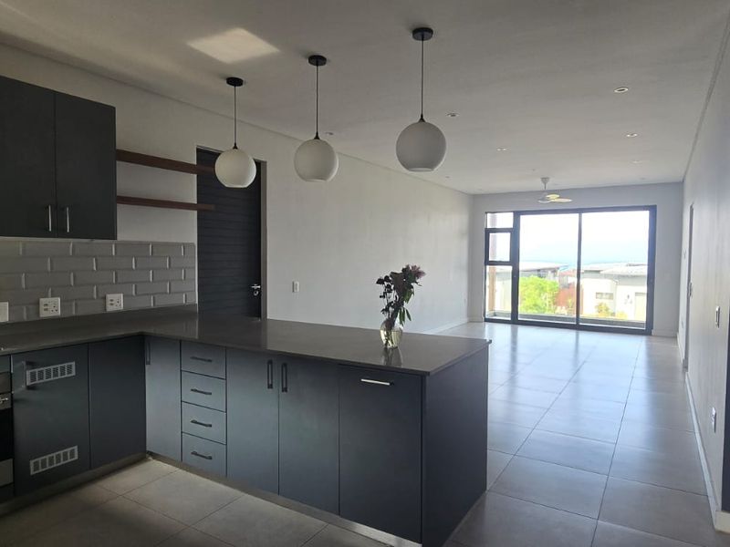 Modern open-plan kitchen and living area featuring dark cabinetry, stone countertops, integrated appliances, and large sliding doors leading to an outdoor space.