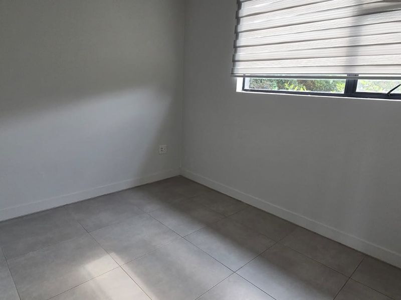 A clean, empty bedroom featuring neutral tiled flooring, a built-in cupboard, and a modern roller blind, offering a versatile space ready for furnishing.