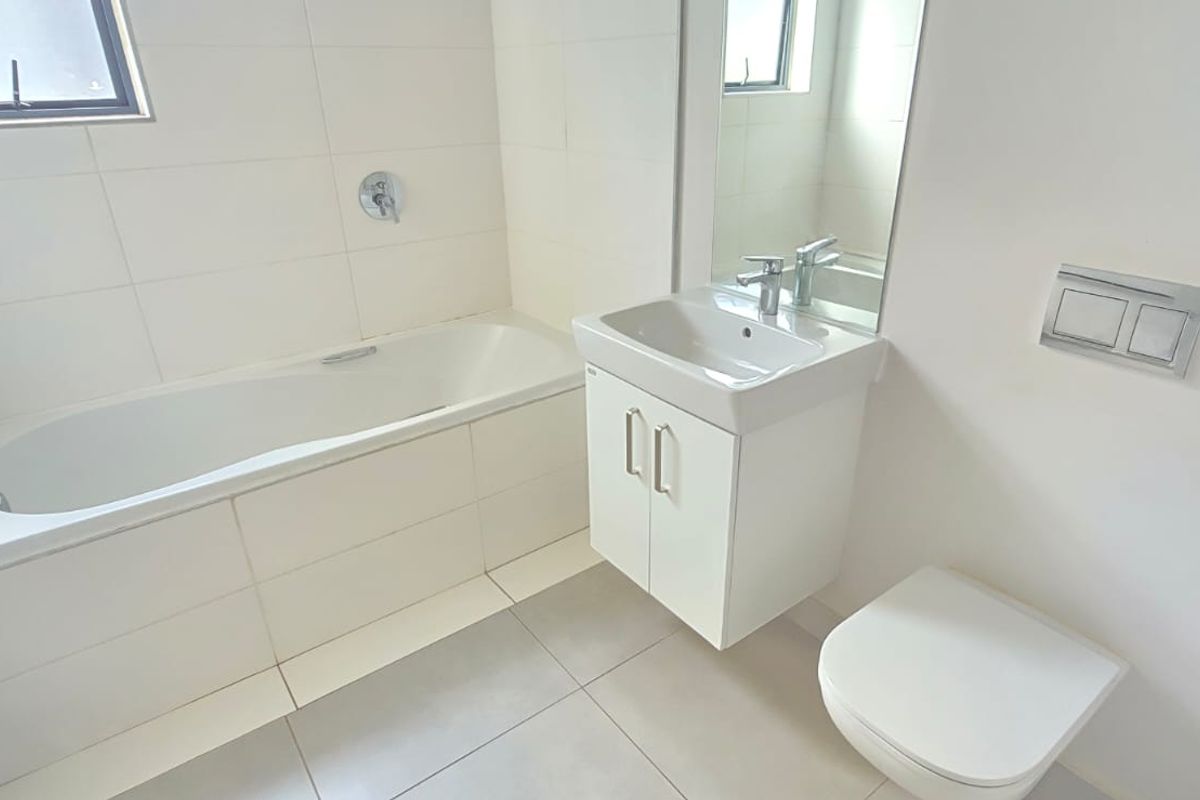 A clean, modern bathroom featuring a built-in bathtub, wall-mounted toilet with concealed cistern, and a vanity basin with storage.