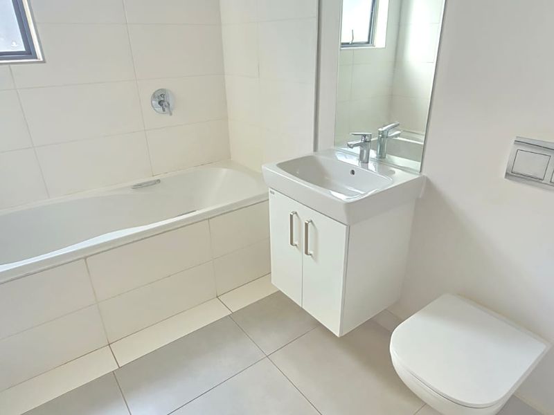 A clean, modern bathroom featuring a built-in bathtub, wall-mounted toilet with concealed cistern, and a vanity basin with storage.