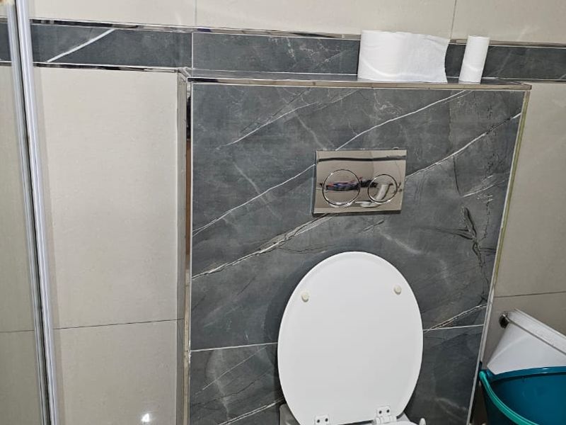 A modern bathroom featuring a wall-mounted toilet with a concealed cistern, chrome flush plate, and contemporary tiled wall finishes.