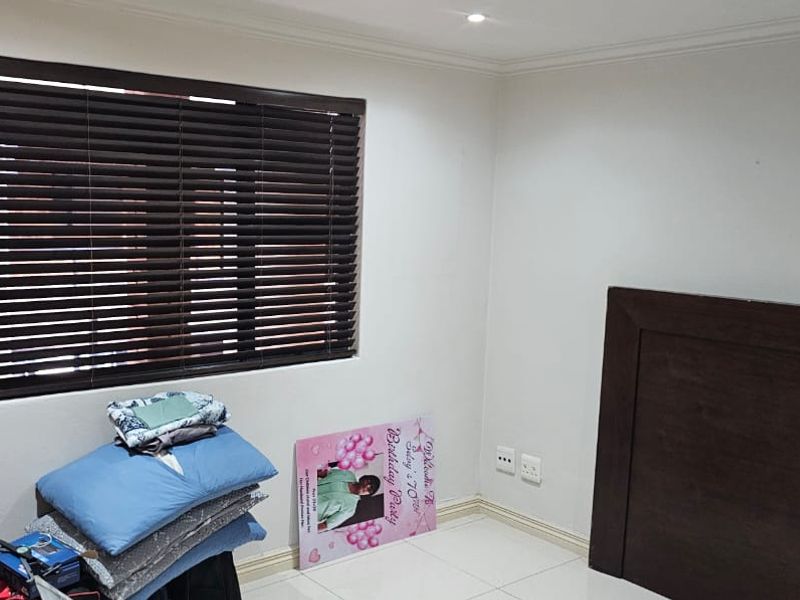A clean, neutral bedroom featuring tiled flooring, recessed lighting, and dark venetian blinds, offering a blank canvas for personalization.
