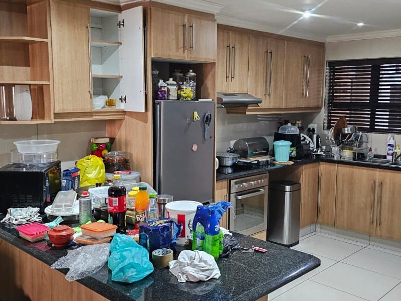 A functional kitchen featuring wood-finish cabinetry, granite countertops, integrated oven, extractor fan, and tiled flooring with direct access to an outdoor balcony area.