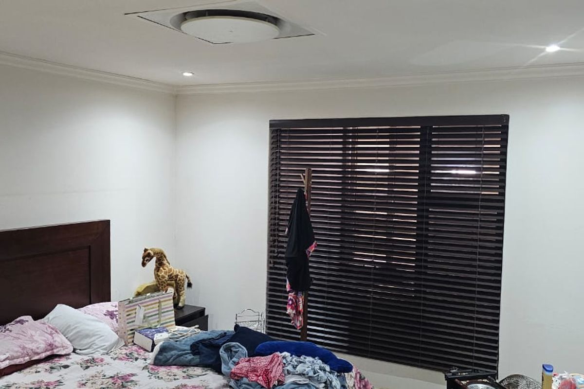 A well-lit bedroom featuring recessed ceiling lights, dark venetian blinds, and a wall-mounted television bracket.