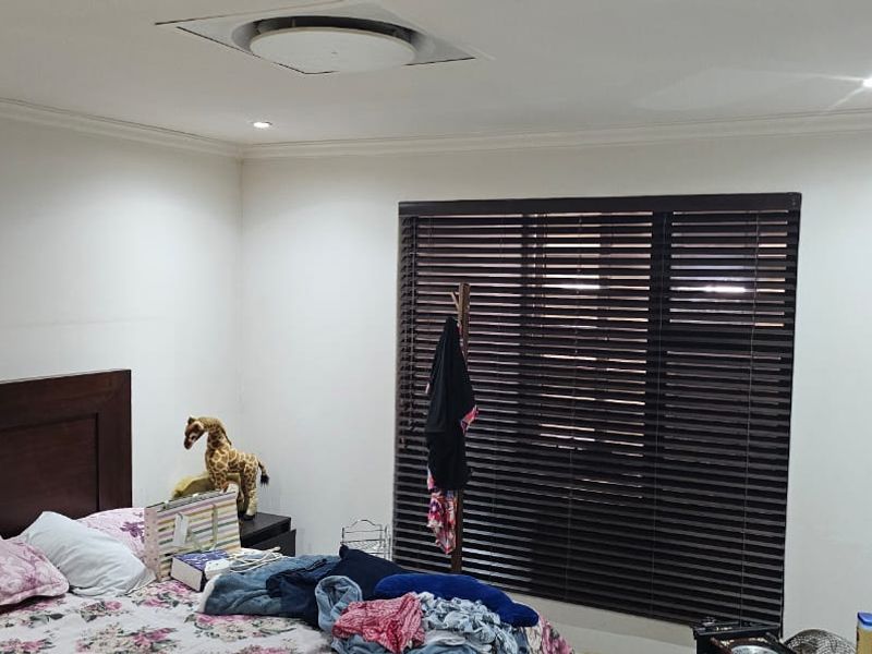 A well-lit bedroom featuring recessed ceiling lights, dark venetian blinds, and a wall-mounted television bracket.
