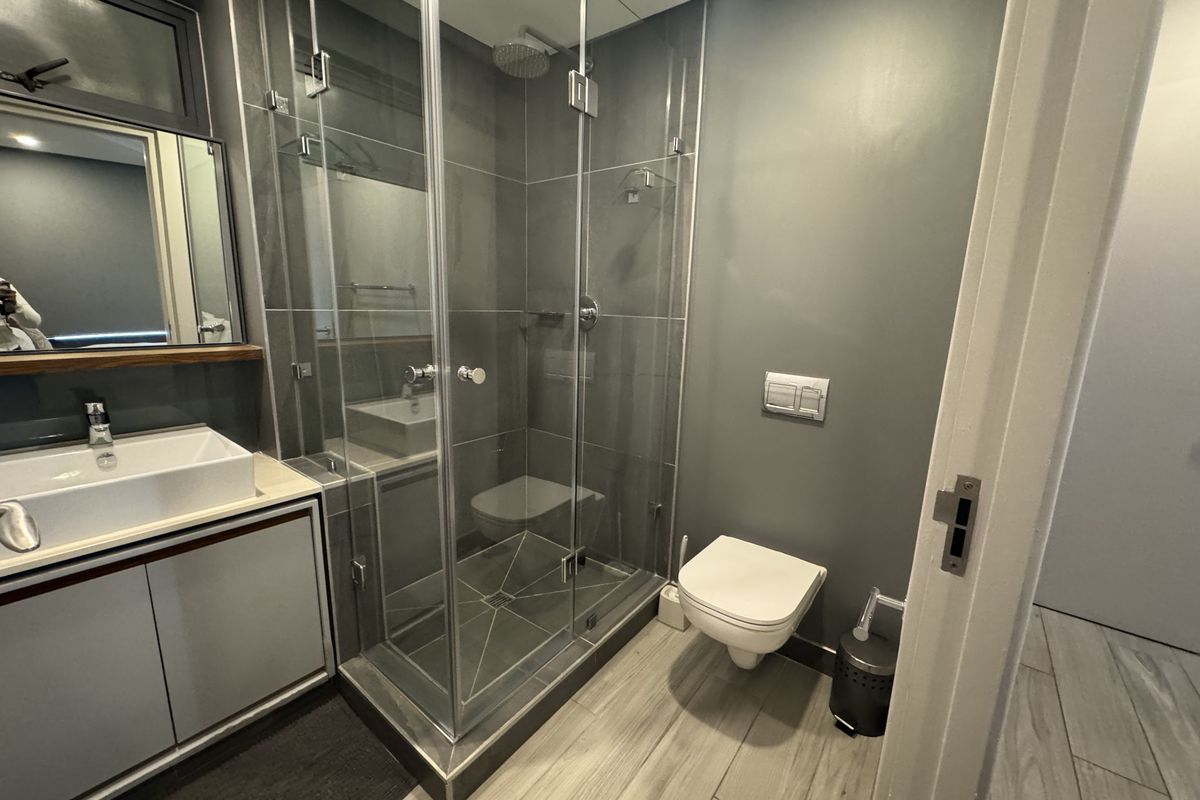 Modern bathroom featuring a glass-enclosed shower, wall-mounted toilet, and a sleek vanity with a vessel sink, finished with contemporary grey tiling.