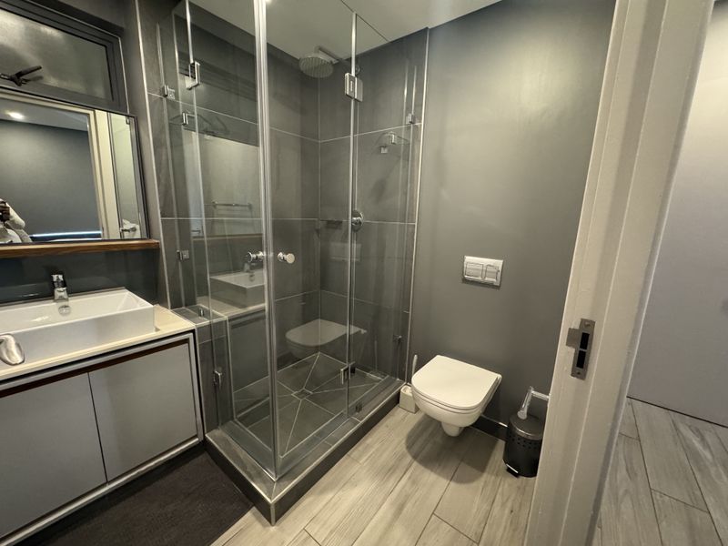 Modern bathroom featuring a glass-enclosed shower, wall-mounted toilet, and a sleek vanity with a vessel sink, finished with contemporary grey tiling.