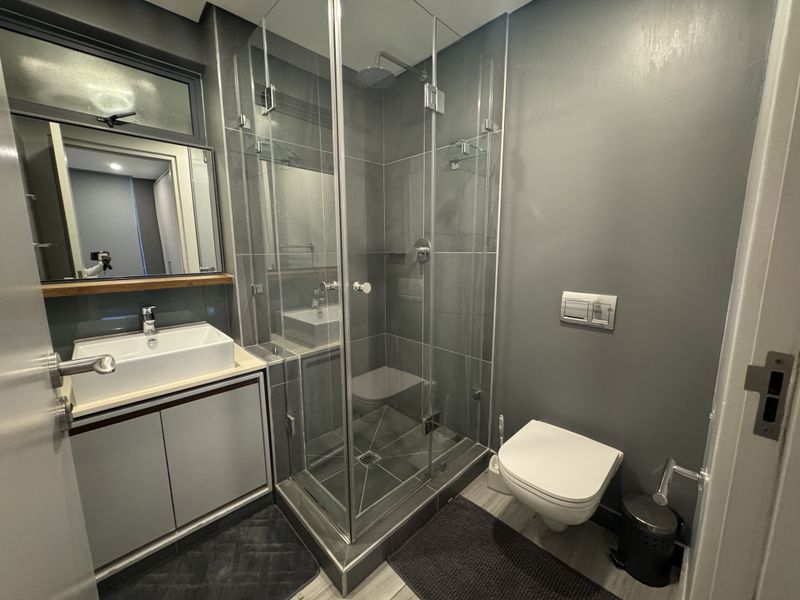 Modern bathroom featuring a glass-enclosed shower, wall-mounted toilet, and a sleek vanity with a vessel sink and contemporary finishes.