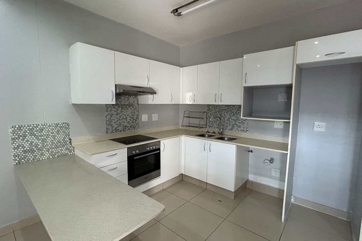 A clean, modern kitchen featuring white cabinetry, stone countertops, a mosaic backsplash, and integrated appliances including an oven and hob.