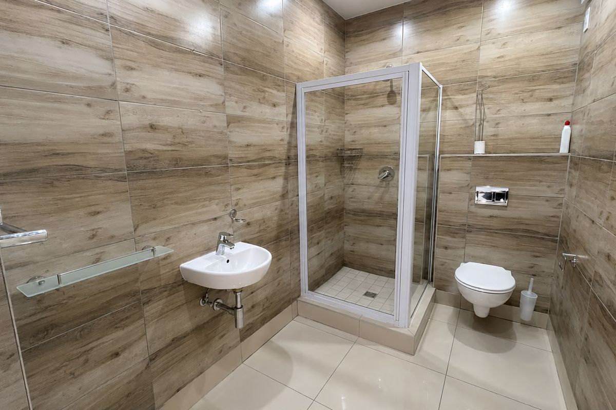 Modern bathroom featuring wood-look wall tiling, a wall-mounted basin, a glass-enclosed shower, and a wall-hung toilet with a concealed cistern.