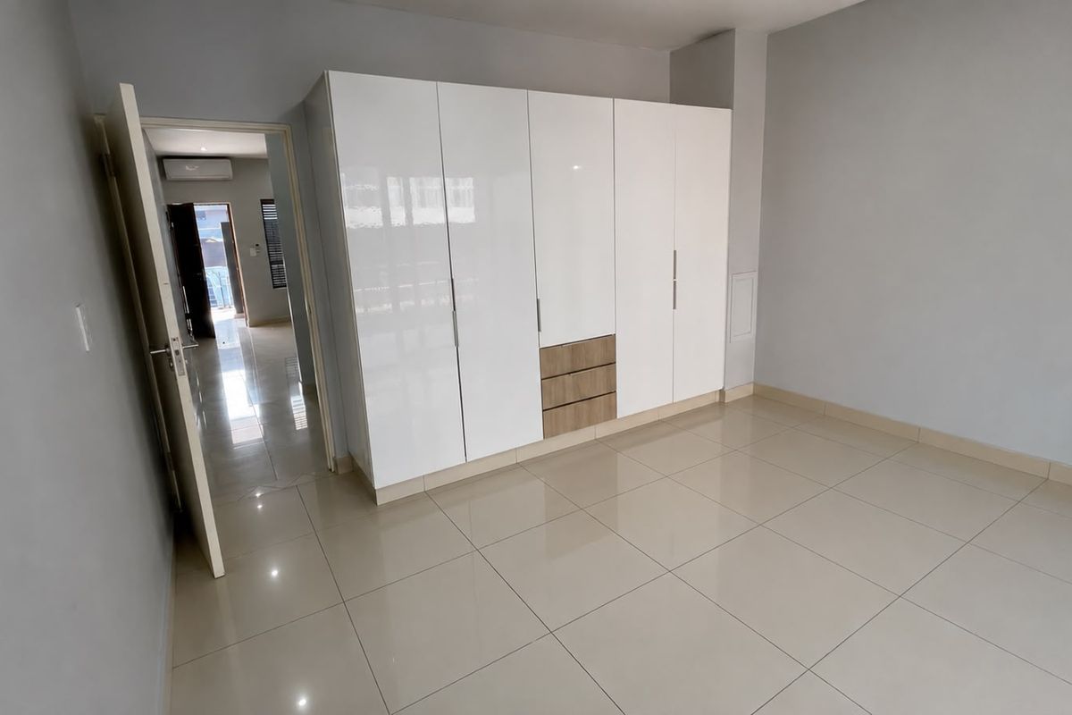 A bright, empty bedroom featuring modern high-gloss built-in cupboards and neutral tiled flooring, offering a clean and versatile living space.