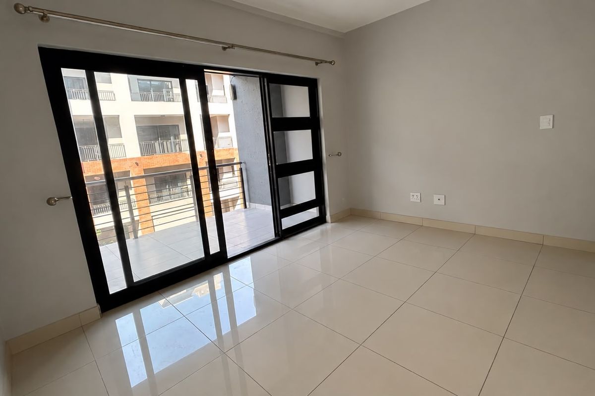 A bright, empty living area featuring large format floor tiles, neutral walls, and a sliding glass door providing access to a private balcony.