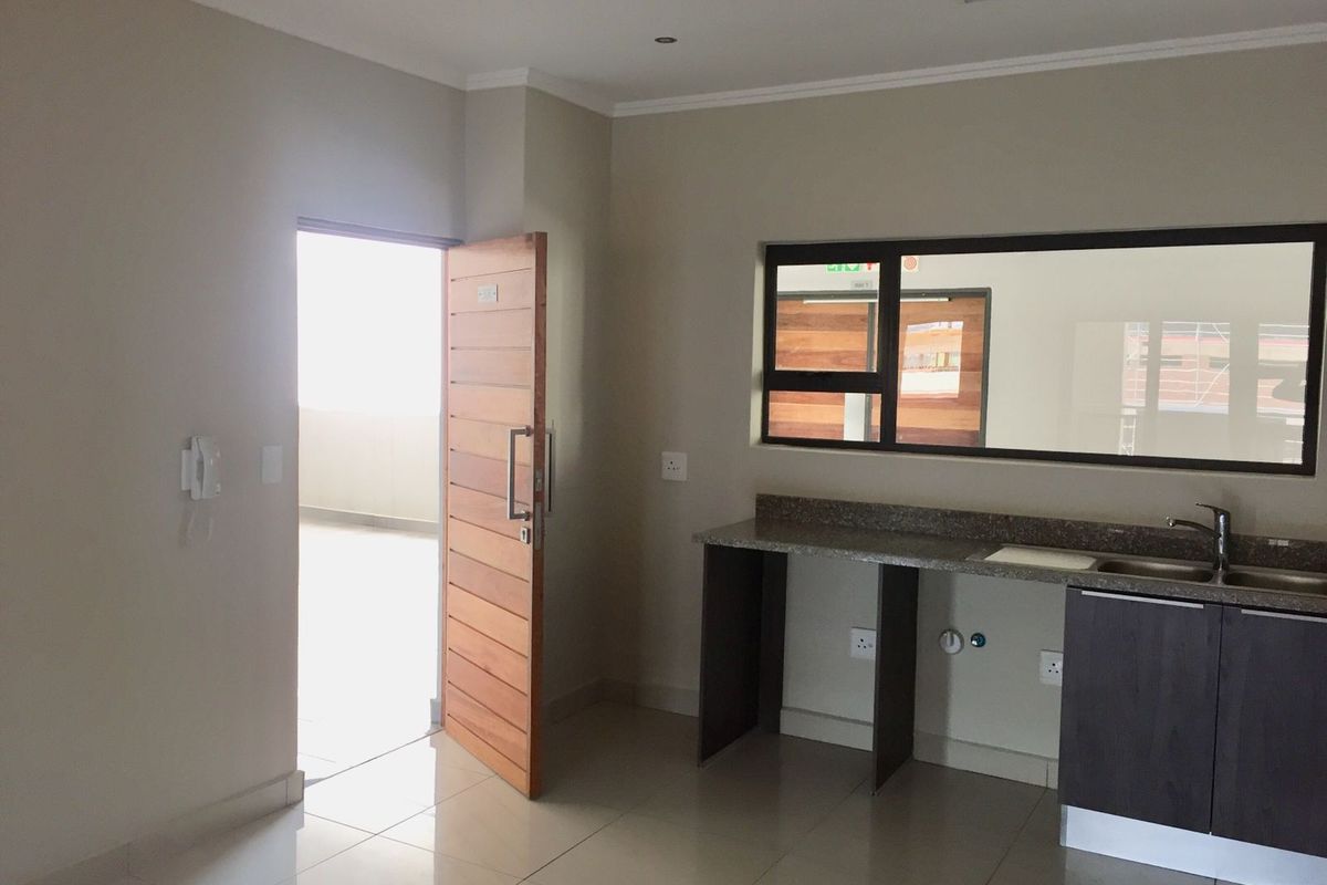 A clean, empty kitchen area featuring granite countertops, a stainless steel sink, and modern tiled flooring with direct access to an outdoor space.