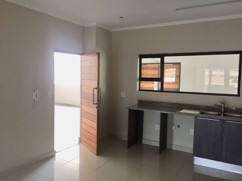 A clean, empty kitchen area featuring granite countertops, a stainless steel sink, and modern tiled flooring with direct access to an outdoor space.