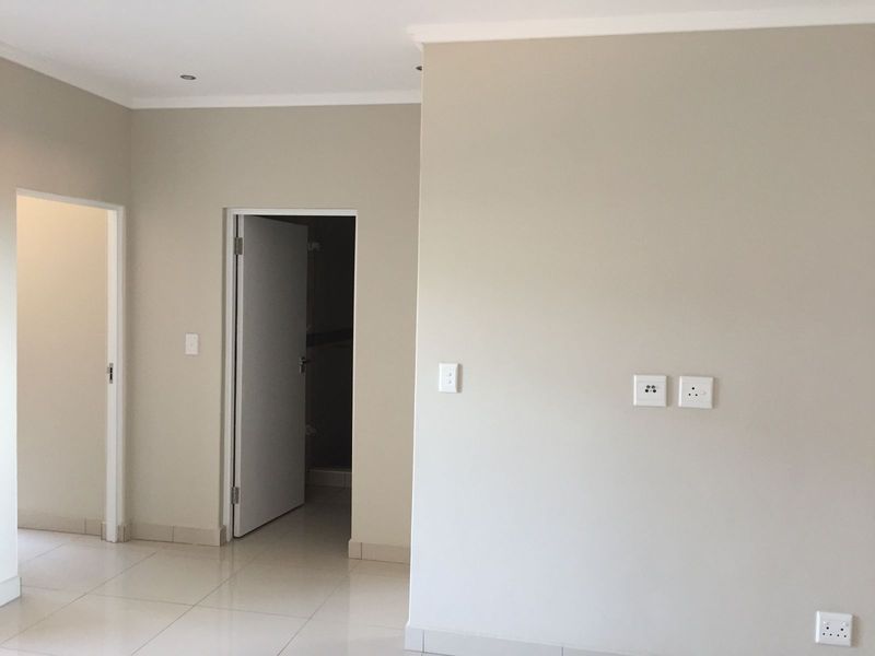 A clean, neutral-toned hallway featuring tiled flooring, recessed downlighting, and multiple electrical access points, providing a bright and functional transition space.