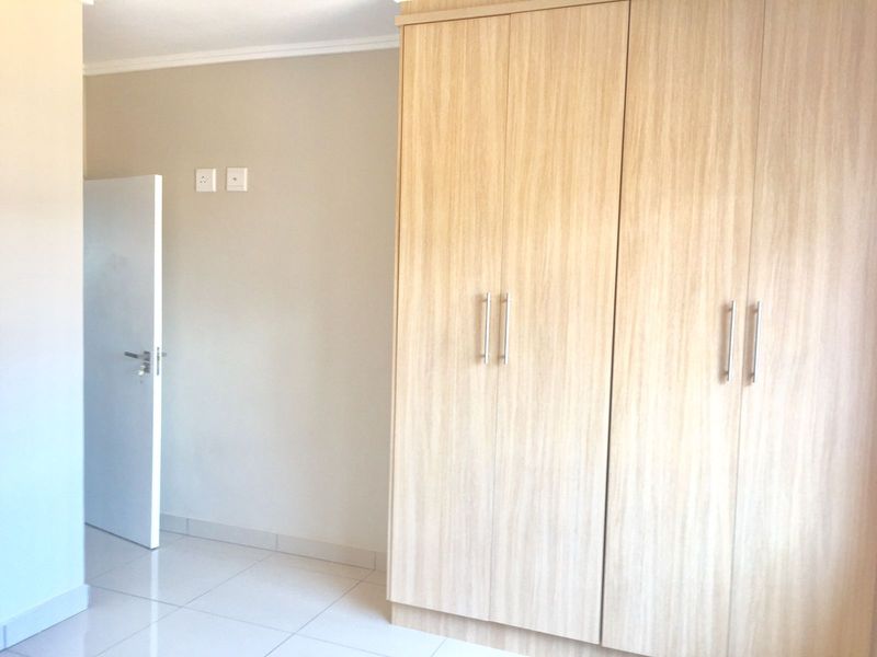 A clean, bright bedroom featuring light wood-finish built-in cupboards and neutral tiled flooring.