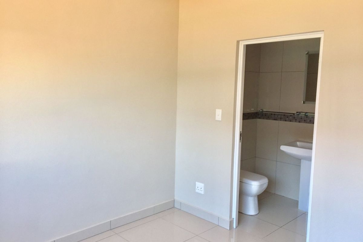 A clean, empty bedroom featuring neutral tiled flooring and an en-suite bathroom with a pedestal basin and toilet.
