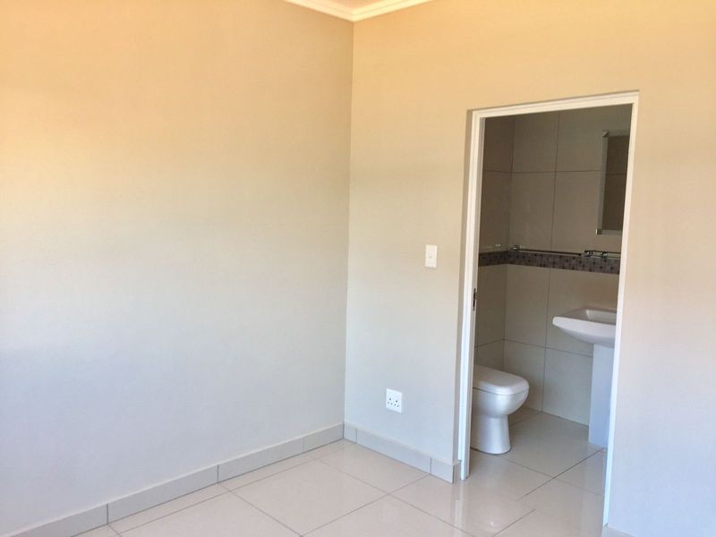 A clean, empty bedroom featuring neutral tiled flooring and an en-suite bathroom with a pedestal basin and toilet.