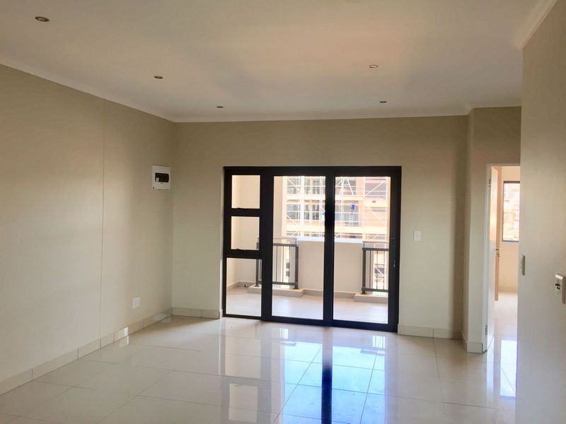 A bright, empty living room featuring neutral walls, polished tiled flooring, recessed lighting, and a sliding door leading to a private balcony.