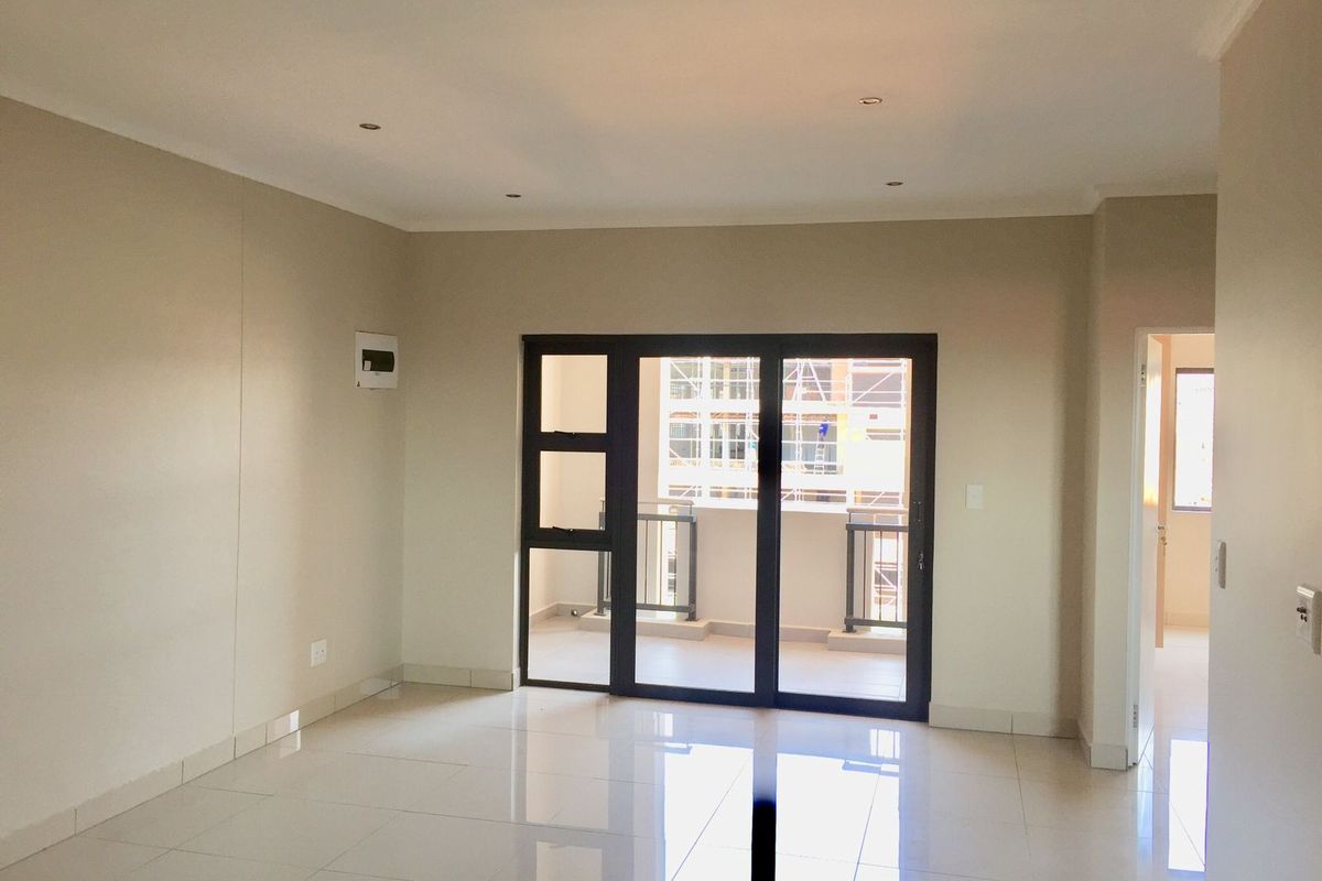 A bright, empty living room featuring polished floor tiles, recessed lighting, and a large aluminium sliding door providing access to a balcony.