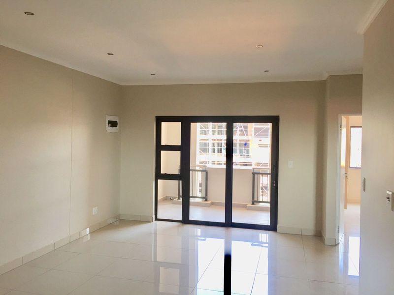 A bright, empty living room featuring polished floor tiles, recessed lighting, and a large aluminium sliding door providing access to a balcony.