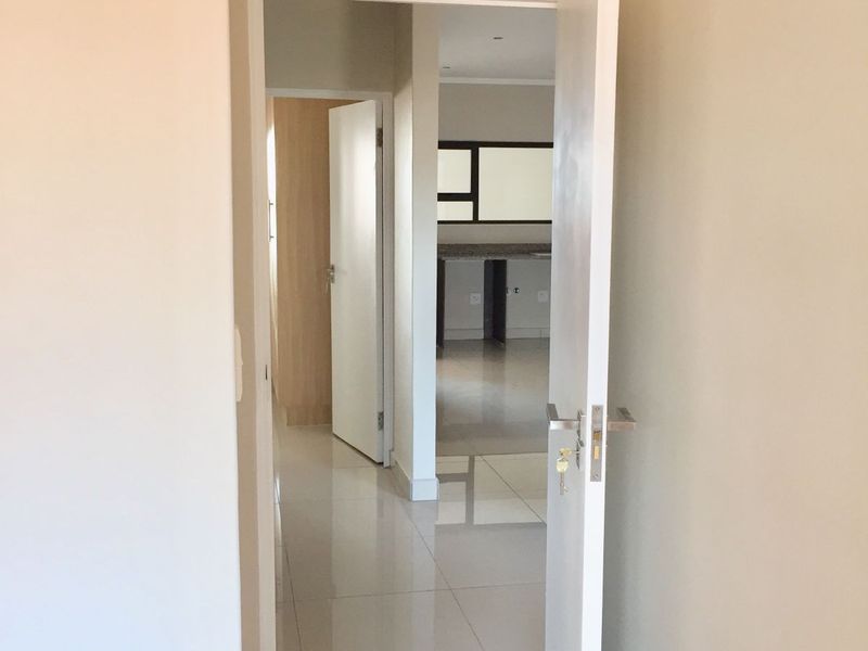 A bright, neutral hallway with tiled flooring leading through to an open-plan living and kitchen area.