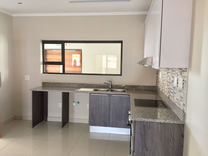 Modern kitchen featuring granite countertops, built-in cabinetry, an electric hob with extractor fan, and a mosaic tile backsplash.