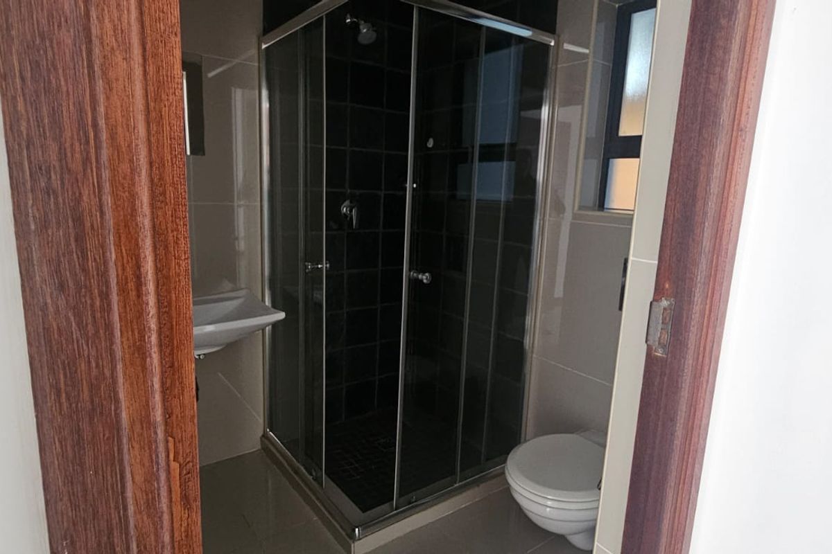 A compact bathroom featuring a corner shower enclosure, wall-mounted basin, and toilet with neutral wall and floor tiling.