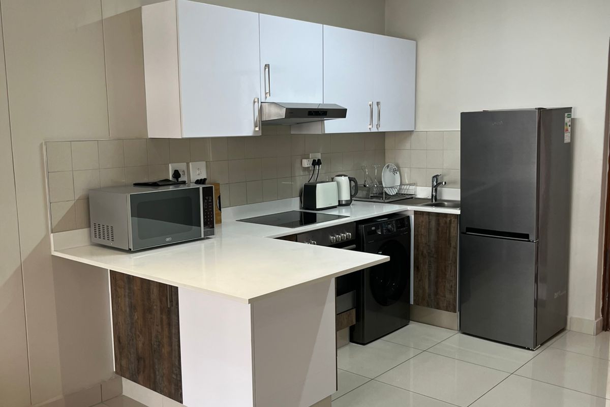 Modern kitchen featuring white and wood-grain cabinetry, quartz countertops, tiled backsplash, and integrated appliances including an oven and hob.