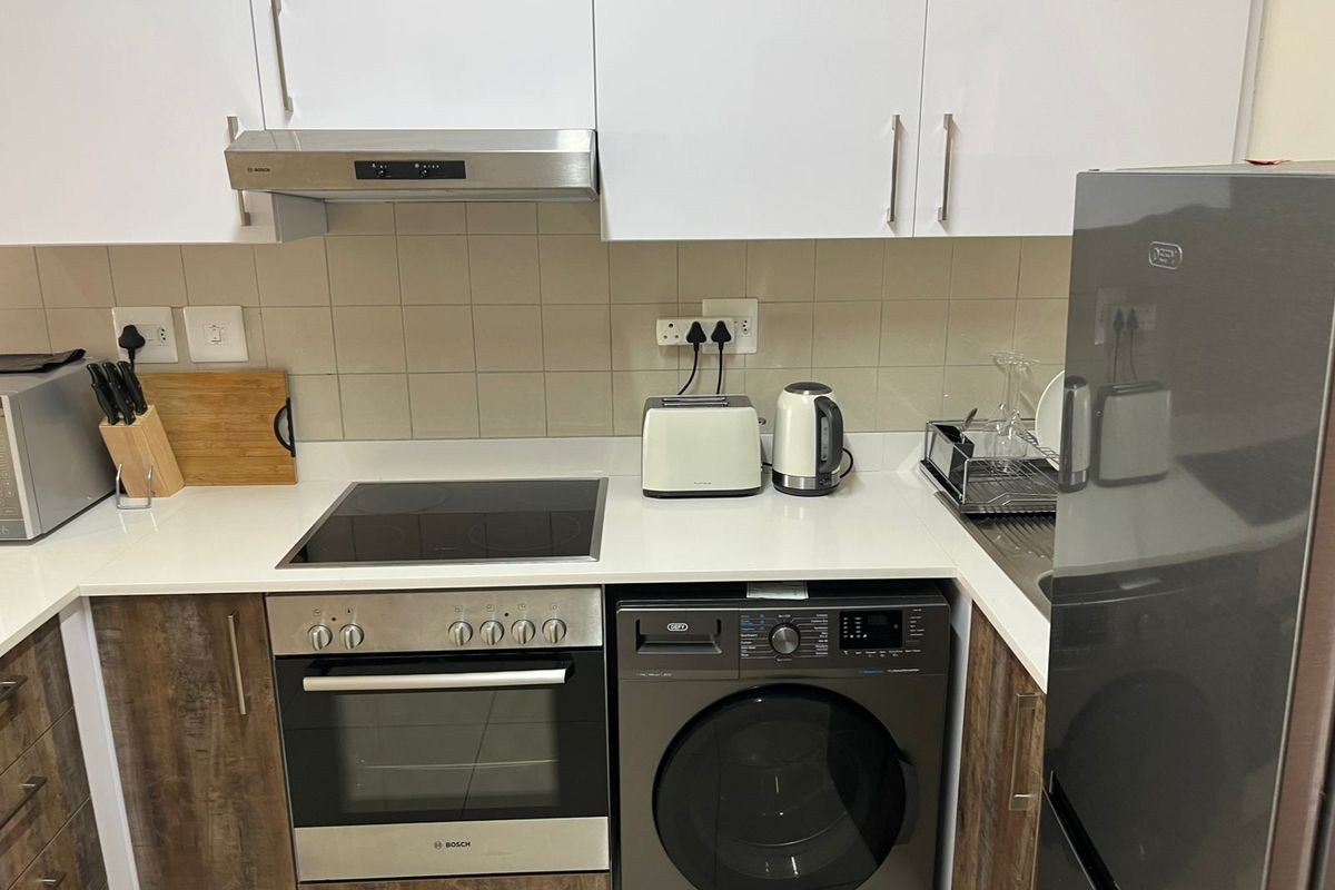 Modern kitchen featuring white upper cabinets, wood-grain lower cabinetry, quartz countertops, a built-in oven, electric hob, and an integrated washing machine.
