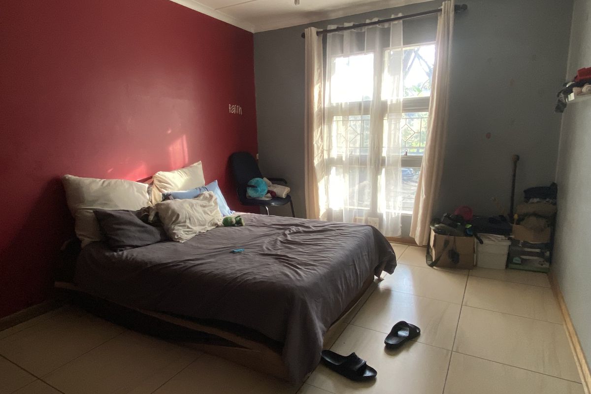 A bedroom featuring large windows with security gates and tiled flooring, offering a functional space with potential for cosmetic updates.