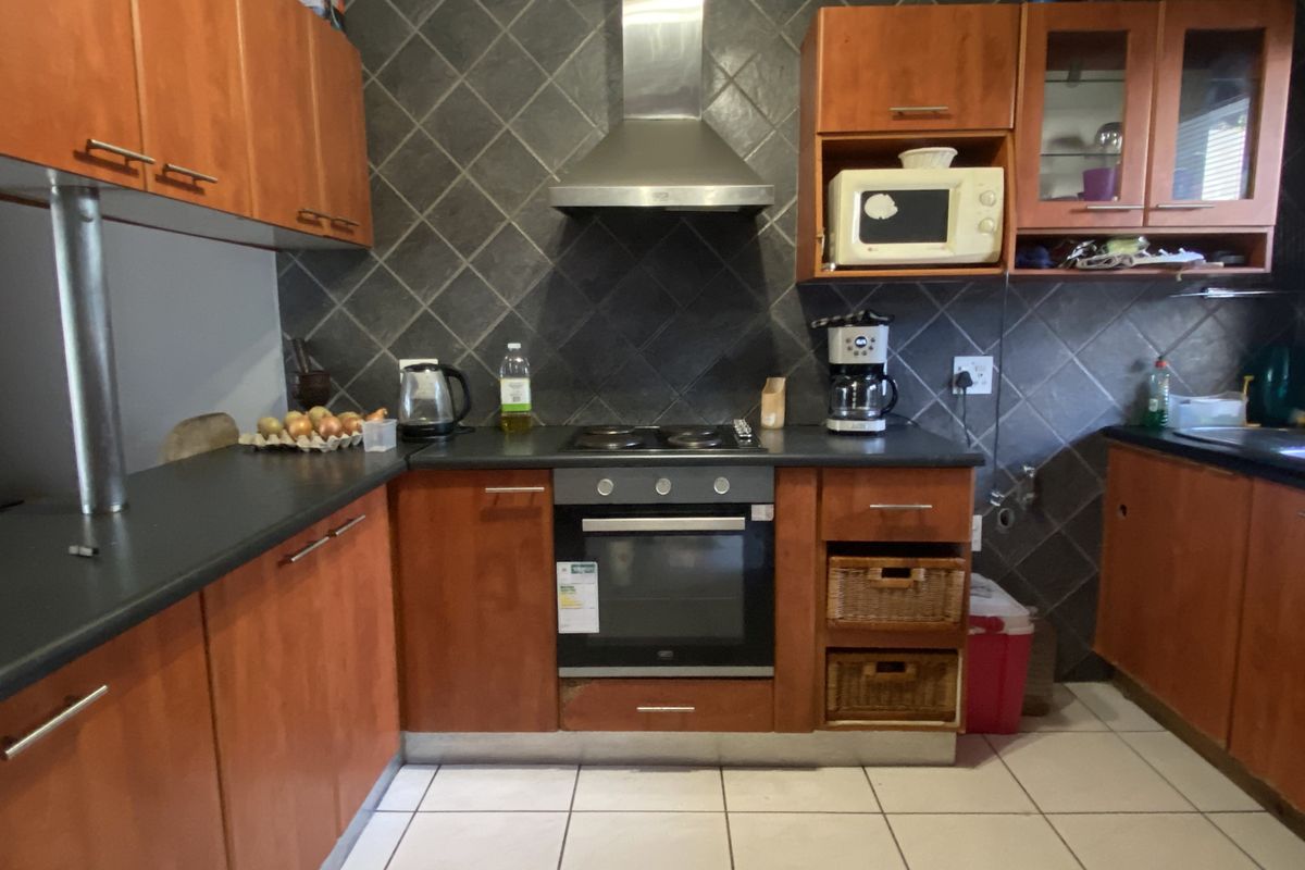 A functional kitchen featuring wooden cabinetry, dark tiled backsplash, built-in oven, and electric hob with a stainless steel extractor fan.