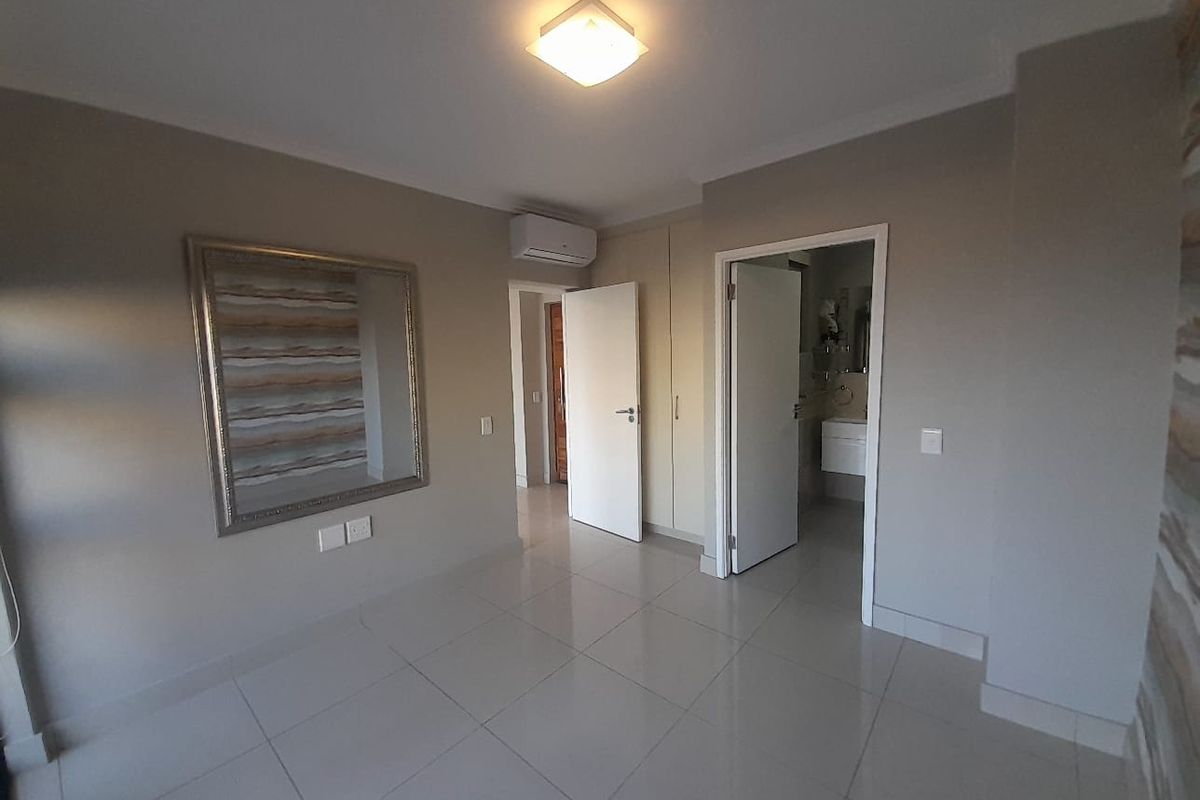 A clean, empty bedroom featuring tiled flooring, built-in cupboards, and an integrated air conditioning unit, with an adjoining en-suite bathroom.