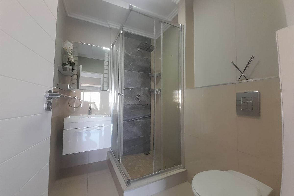Modern bathroom featuring a wall-mounted vanity, glass shower enclosure with rain shower head, and a wall-hung toilet with concealed cistern.