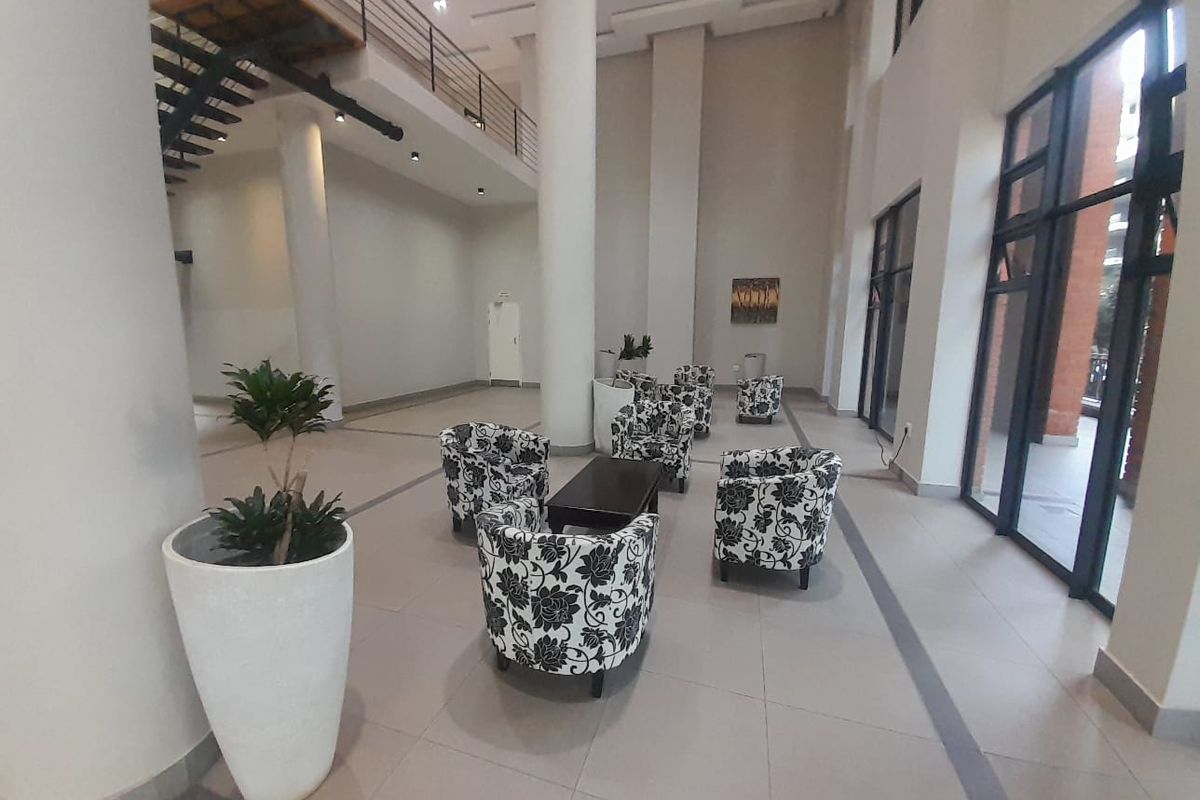 Spacious double-volume living area featuring structural columns, a mezzanine level with a metal staircase, and large glass windows providing ample natural light.