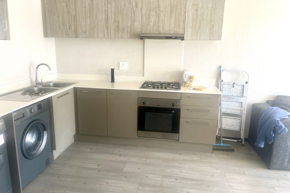 Modern kitchen featuring light wood-tone cabinetry, stainless steel appliances including a gas hob and oven, and integrated laundry facilities.