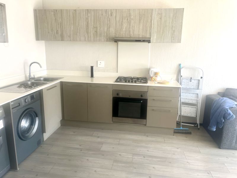 Modern kitchen featuring light wood-tone cabinetry, stainless steel appliances including a gas hob and oven, and integrated laundry facilities.
