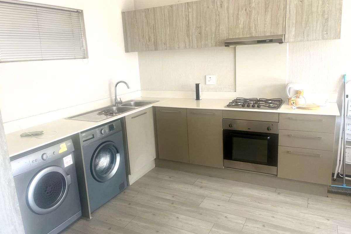 Modern kitchen featuring light wood-tone cabinetry, integrated gas hob, built-in oven, extractor fan, and durable laminate flooring with ample counter space.