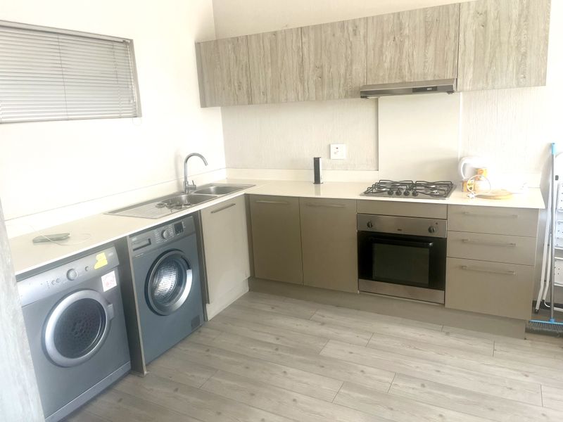 Modern kitchen featuring light wood-tone cabinetry, integrated gas hob, built-in oven, extractor fan, and durable laminate flooring with ample counter space.