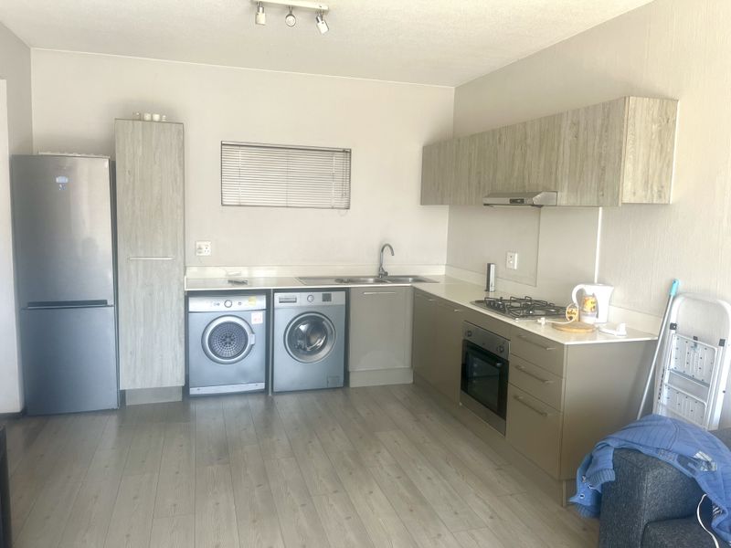 A functional kitchen featuring light wood-look cabinetry, integrated gas hob, oven, extractor fan, and space for laundry appliances with modern laminate flooring.